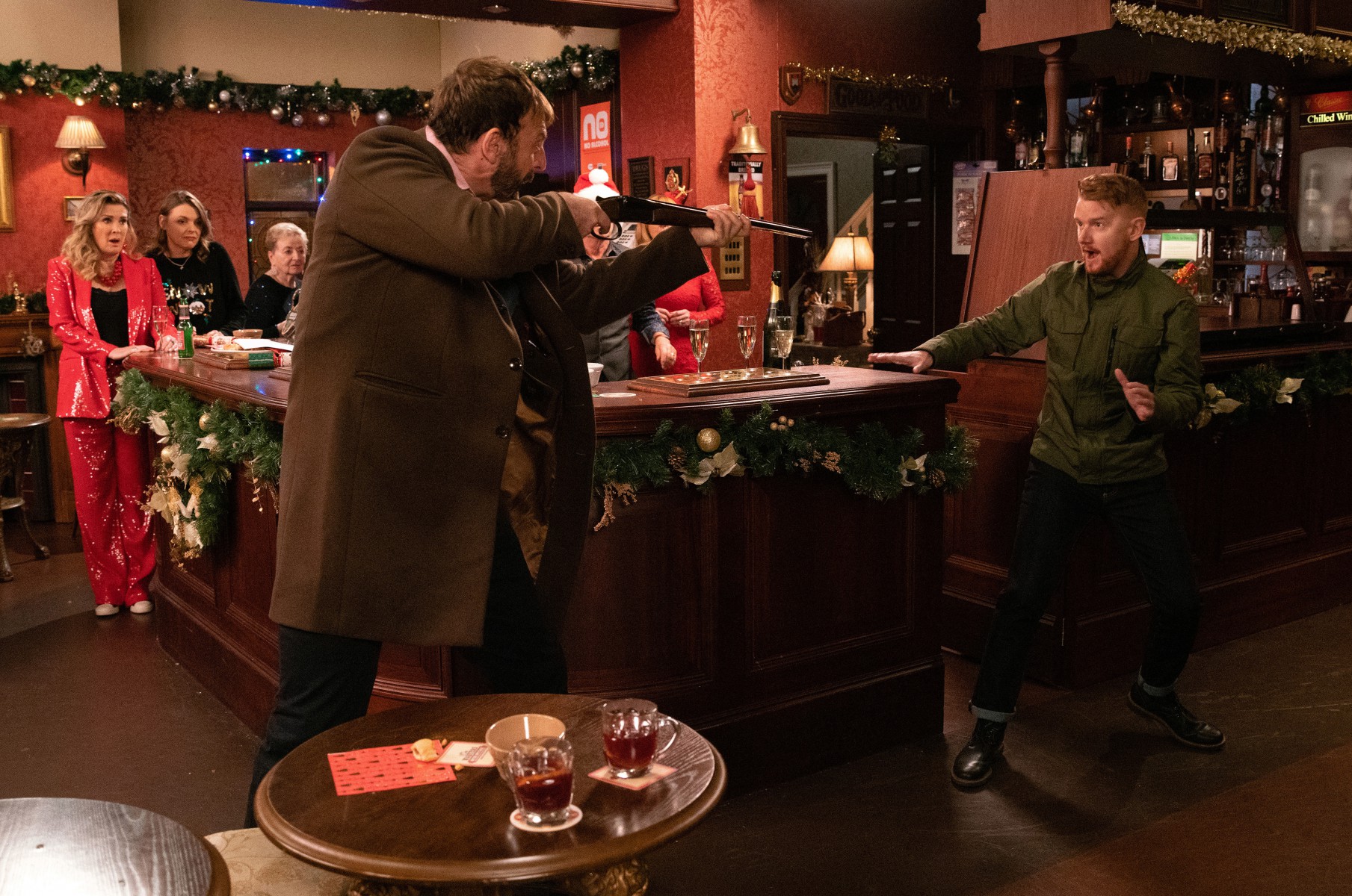 The pub punters are horrified as Derek holds Gary at gunpoint in Corrie
