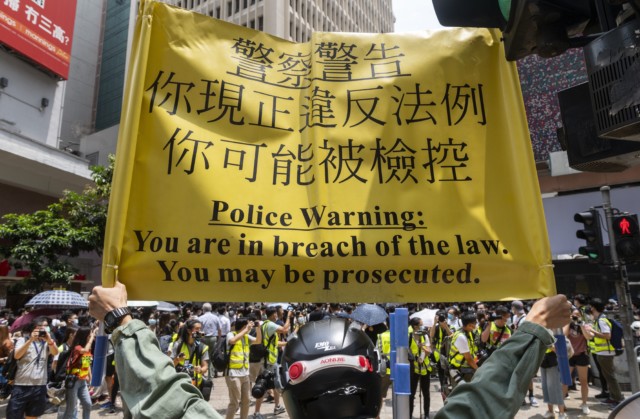A police officer  in Hong Kong holds a yellow banner warning the public to be prosecuted if they continue to gather