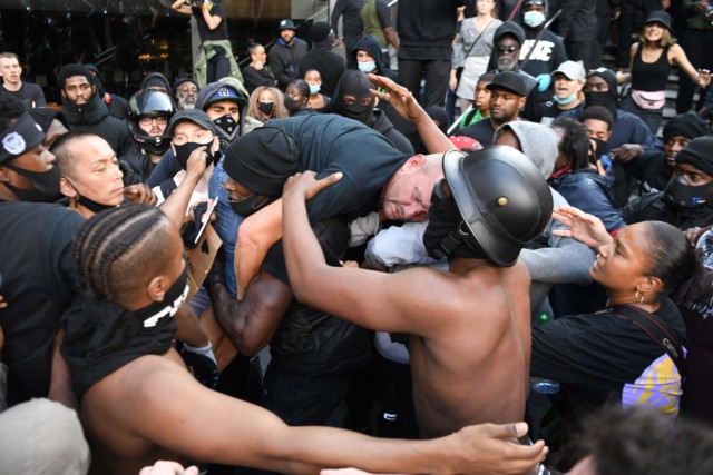 A member of BLM carries a man from the counter protest to police after he was punched