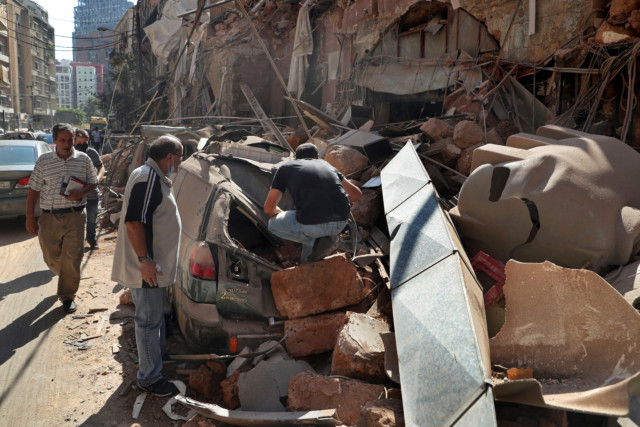 People check inside a car crushed by rubble 